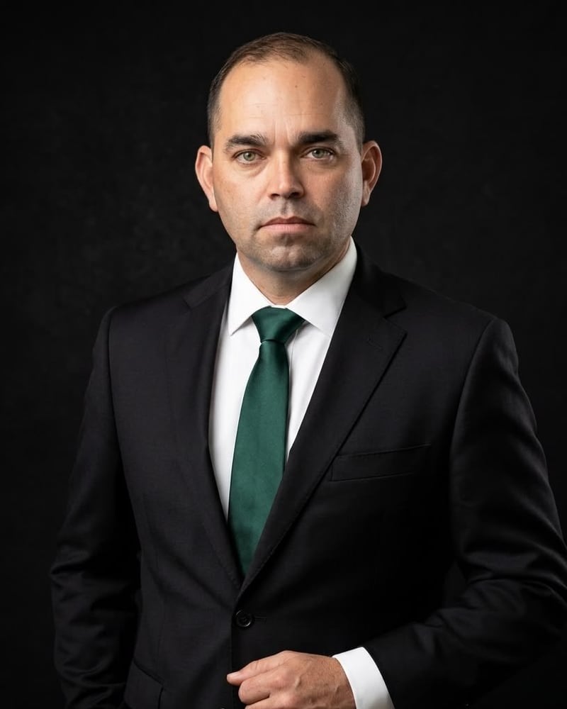 Gibrán González de traje negro y corbata verde, en un retrato de estudio